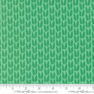 May include: Green fabric with a repeating pattern of stylized leaves. The leaves are a darker shade of green against a lighter green background. A ruler is at the bottom, with the word "moda" printed on it.