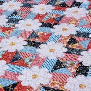 Pode incluir: Um padrão de colcha intitulado "blossoms" com um desenho de margarida branca sobre um fundo de patchwork vermelho, azul e preto. O padrão é descrito como "um padrão de colcha amigável para 10 quadrados de Amanda Murphy Design."
