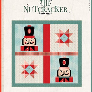 Könnte beinhalten: Ein kostenloses Muster für eine Steppdecke mit einem Nussknacker-Motiv. Die Steppdecke besteht aus vier Quadraten, jedes mit einem anderen Design. Das obere linke Quadrat zeigt einen Nussknacker, das obere rechte Quadrat zeigt einen Stern, das untere linke Quadrat zeigt einen Stern und das untere rechte Quadrat zeigt einen Nussknacker. Die Steppdecke ist aus roten, weißen und blauen Stoffen gefertigt.