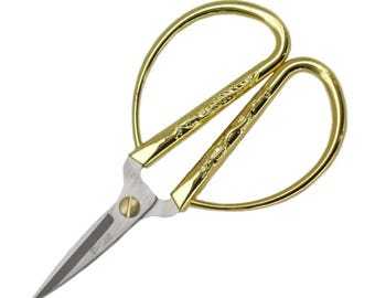 May include: Gold-colored scissors with a stainless steel blade. The handles are a bright gold color with a decorative etched design. The blades are sharp and pointed, and the word "STAINLESS" is printed on the blade.