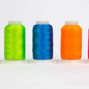 Könnte beinhalten: Fünf Spulen mit neonfarbenem Garn. Die Spulen sind von links nach rechts angeordnet: gelb, grün, blau, orange und pink.