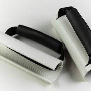 May include: Two white and black stroller handles with black foam grips and black fabric straps. The handles are curved and designed to attach to a stroller frame. The background is white.