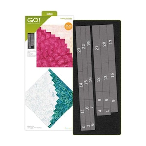 May include: A GO! Fabric Cutting Die for a curved log cabin quilt pattern, featuring a rectangular black foam board with numbered cutouts from 1 to 23. The packaging displays a pink and teal geometric quilt design with the text GO! and BOB.