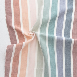 Puede incluir: Una tela de rayas coloridas con un patrón de arcoíris en tonos de rosa, naranja, verde, azul y morado. La tela está doblada y tiene un fondo blanco.