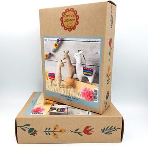 May include: A brown craft kit box displaying felt llamas. The box is labelled "Corinne Lapierre Made in Britain." The kit includes beige and white felt llamas with colourful saddle blankets. The box is decorated with floral patterns.