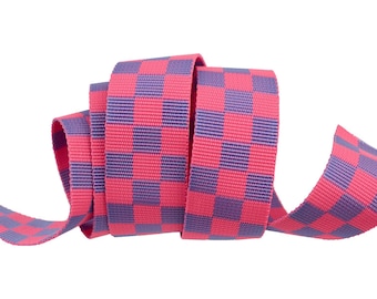 May include: A length of pink and purple checkered ribbon, curled against a white backdrop. The ribbon features a grid pattern of alternating pink and purple squares. This ribbon is likely used for crafts or gift wrapping.