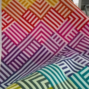 May include: A colorful quilt with a geometric pattern of stripes and squares in shades of yellow, orange, red, pink, purple, blue, and green.