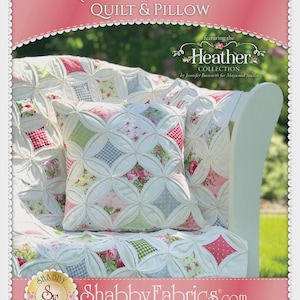 May include: A quilted pillow and quilt set with a floral pattern, displayed on a white chair. The quilt and pillow feature a "Cathedral Window" design with pink, green, and white fabrics. The image includes the text "Cathedral Window QUILT & PILLOW" and "Shabby Fabrics.com".