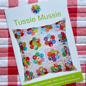 May include: A white card with the text "Tussie Mussie" and a colorful patchwork cushion design. The finished cushion size is 16" x 16". The card is on a red and white checkered surface.