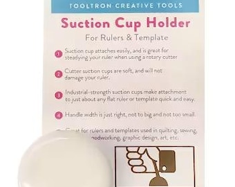 May include: A white suction cup holder for rulers and templates. The product packaging includes the text "TOOLTRON CREATIVE TOOLS Suction Cup Holder For Rulers & Template". The holder is designed for quilting, sewing, and graphic design.