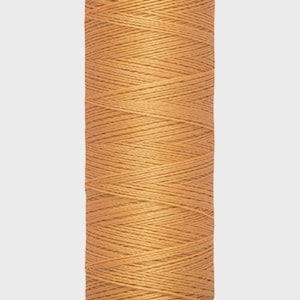 May include: A spool of Gütermann thread in a warm, golden-brown hue. The label reads "Gütermann" at the top and "100 m - 110 yds/vgs" at the bottom. The thread is tightly wound, showcasing its texture and quality.