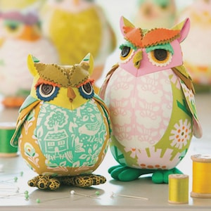 May include: Two colorful owl pincushions with button eyes and patterned fabric. One owl is yellow and teal, the other pink and green. The text "Heather Bailey Sewing Patterns" and "edgar owl & poe Pincushions" are visible.