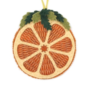 May include: A felt orange slice ornament with a yellow hanging ribbon. The ornament features a light orange center with a cream-colored rind and green felt leaves. The orange slice is approximately 4 inches in diameter.