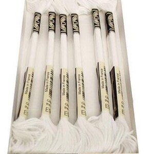 May include: A box of white embroidery floss. The floss is labeled "Made in France" and "Glow in the dark". The spools have black and gold accents. The box is white and beige.