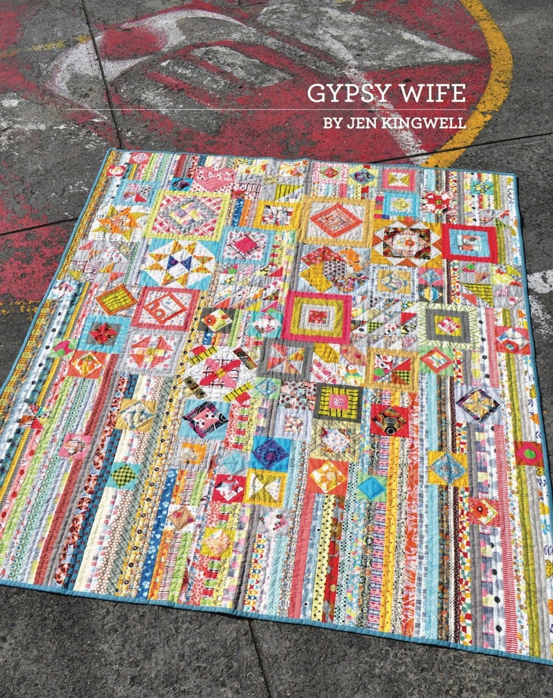 Puede incluir: Una colcha colorida con una variedad de patrones y colores, incluyendo rojo, amarillo, azul, verde y blanco. La colcha est&aacute; hecha de cuadrados y rect&aacute;ngulos, y tiene un borde azul. La colcha se titula "Gypsy Wife" por Jen Kingwell.