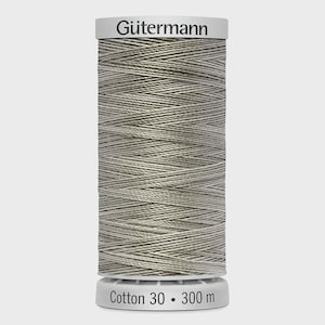 Könnte beinhalten: Eine Spule Gütermann Baumwollgarn in einem neutralen, hellgrauen Farbton. Auf der Spule steht "Cotton 30 • 300 m". Das Garn ist eng gewickelt, wodurch die Textur der Baumwolle sichtbar wird. Die Spule hat einen weißen Deckel und Boden.