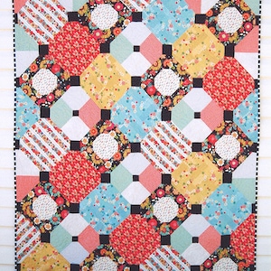 Op de afbeelding: Een quiltpatroon met een geometrisch ontwerp met een verscheidenheid aan kleurrijke stoffen. De quilt is gemaakt van vierkanten en achthoeken in tinten rood, geel, blauw, groen en zwart. Het patroon heet "#303 Just Smashing" en is verkrijgbaar bij AbbeyLaneQuilts.com.