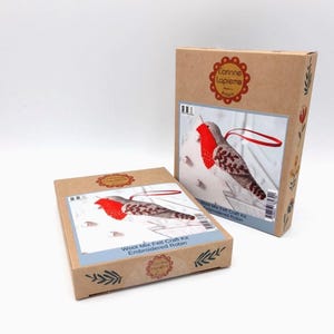 May include: Two brown cardboard boxes containing a red and grey felt craft kit for making an embroidered robin. The boxes have the text "Wool Mix Felt Craft Kit Embroidered Robin" and "Wool Mix Felt Craft Kit Embroidered Robin" printed on them.