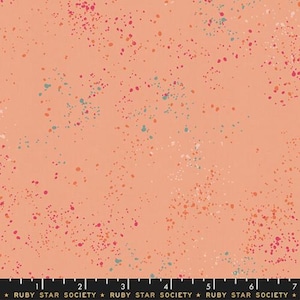 May include: Peach-colored fabric with a speckled pattern. The fabric is covered in small, irregular dots of various colors, including pink, orange, teal, and white. The dots are scattered across the surface, creating a playful and artistic design.