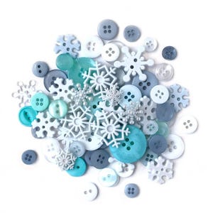 May include: A collection of assorted buttons and snowflake embellishments in shades of white, blue, and teal. The buttons vary in size and shape, with some featuring four holes and others having a two-hole design. The snowflakes are made of plastic.