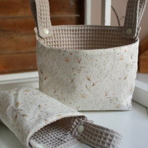 May include: Two beige fabric storage baskets with white floral patterns and waffle-textured handles. The larger basket is taller and wider than the smaller basket.