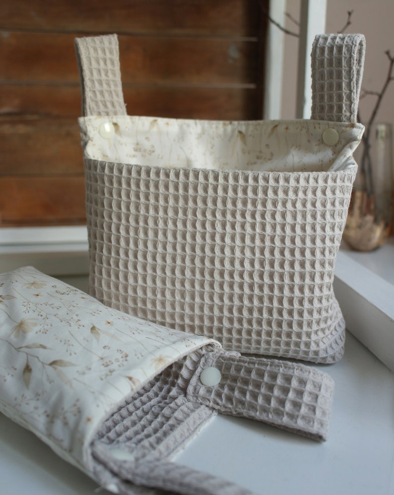 May include: Two beige waffle-weave fabric storage baskets with white floral print lining. The larger basket has two handles and the smaller basket has one handle.