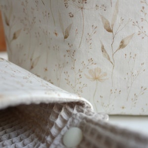 May include: A white fabric storage basket with a brown floral pattern. The basket is made of a soft, natural material and has a simple, elegant design.