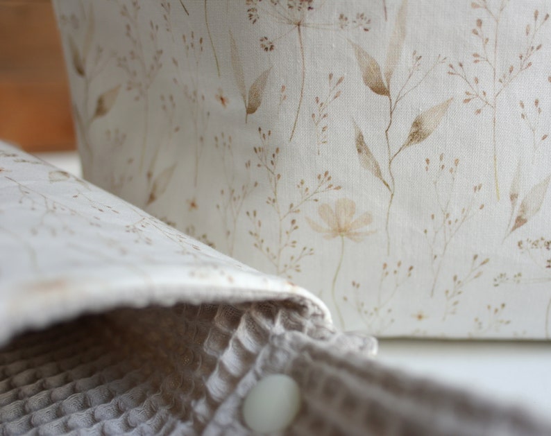 May include: A white fabric storage basket with a brown floral pattern. The basket is made of a soft, natural material and has a simple, elegant design.