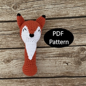 May include: Crochet pattern for a fox rattle toy. The pattern is available as a PDF download. The fox is orange and white with black eyes and a black nose.