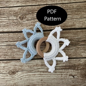 May include: A crochet baby teether with a wooden ring in the center. The teether is made in two colors, light blue and white.