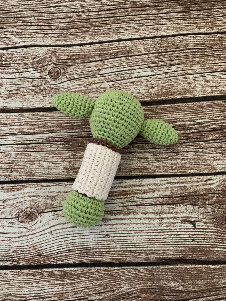 K&ouml;nnte beinhalten: Gr&uuml;nes H&auml;kel-Rassel f&uuml;r Babys in Form einer Figur mit braunen Garn-Akzenten.