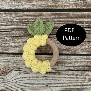 May include: A crocheted pineapple-shaped teether with a wooden ring. The teether is yellow and green and has a PDF pattern.
