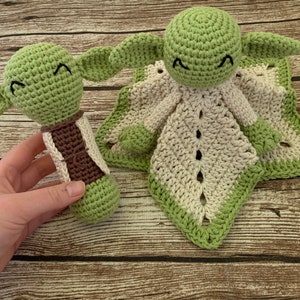 K&ouml;nnte beinhalten: Eine gr&uuml;ne geh&auml;kelte Babyrassel und eine gr&uuml;n-wei&szlig;e geh&auml;kelte Babydecke mit einem l&auml;chelnden Gesicht.
