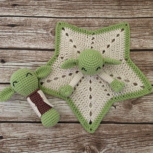 K&ouml;nnte beinhalten: Eine gr&uuml;ne geh&auml;kelte Babydecke in Form eines Sterns mit einer gr&uuml;nen geh&auml;kelten Yoda-Figur in der Mitte. Eine kleinere gr&uuml;ne geh&auml;kelte Yoda-Figur befindet sich auf der linken Seite der Decke.