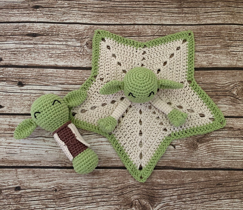 K&ouml;nnte beinhalten: Eine gr&uuml;ne geh&auml;kelte Babydecke in Form eines Sterns mit einer gr&uuml;nen geh&auml;kelten Yoda-Figur in der Mitte. Eine kleinere gr&uuml;ne geh&auml;kelte Yoda-Figur befindet sich auf der linken Seite der Decke.