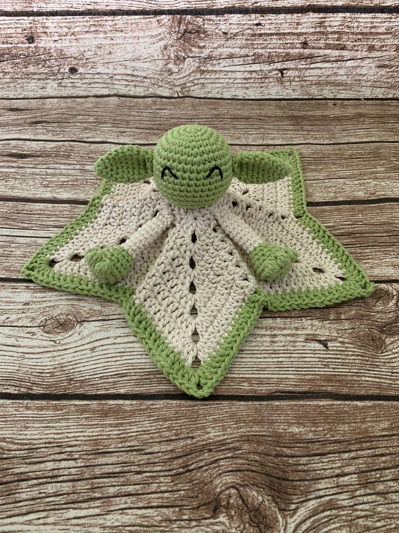 K&ouml;nnte beinhalten: Eine gr&uuml;ne geh&auml;kelte Babydecke mit einer geh&auml;kelten Yoda-Figur in der Mitte. Die Decke ist wei&szlig; mit einem gr&uuml;nen Rand.