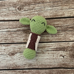 K&ouml;nnte beinhalten: Gr&uuml;nes, geh&auml;keltes Yoda-Rasselspielzeug mit braunen und wei&szlig;en Akzenten.