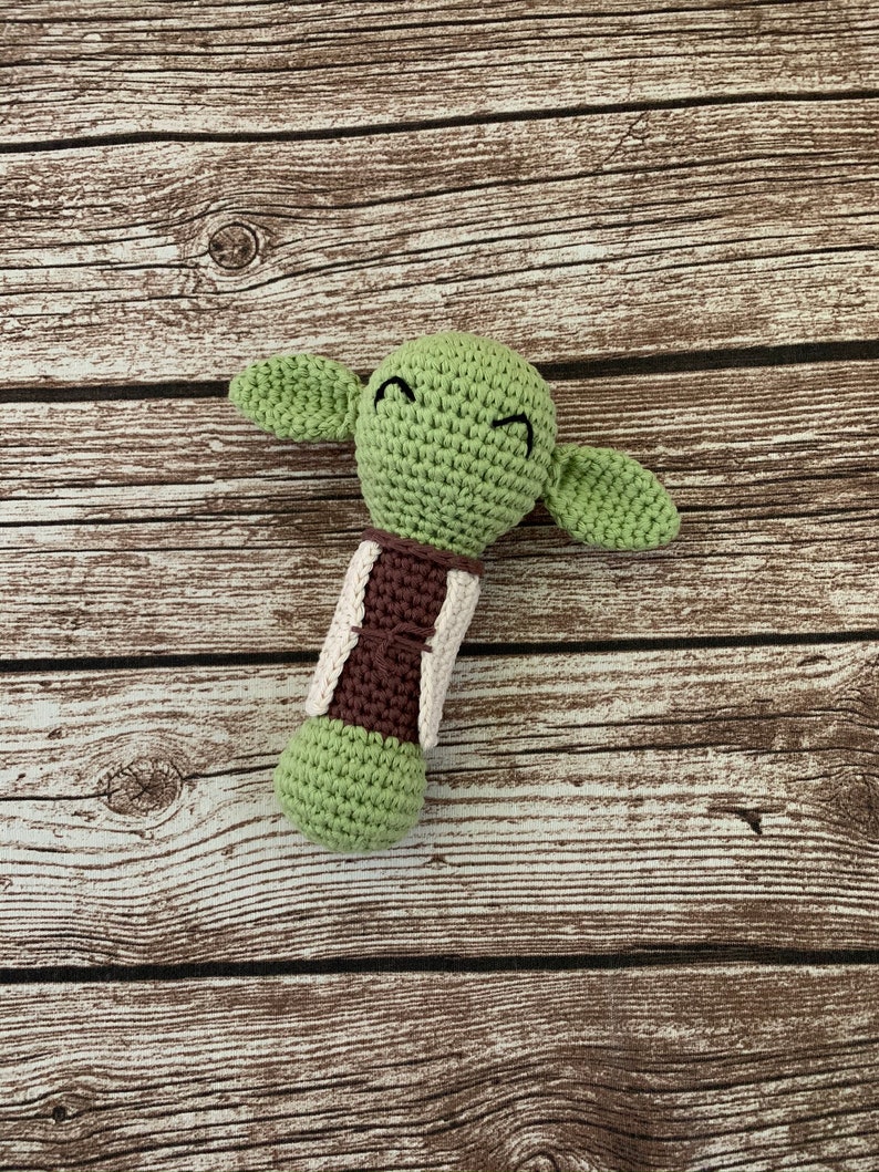 K&ouml;nnte beinhalten: Gr&uuml;nes, geh&auml;keltes Yoda-Rasselspielzeug mit braunen und wei&szlig;en Akzenten.
