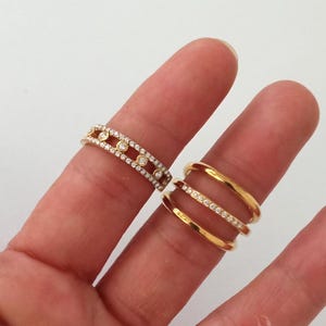Puede incluir: Dos anillos de oro con detalles de diamantes. Uno presenta una banda de diamantes pequeños y grandes. El otro anillo tiene tres bandas, una con diamantes pequeños.