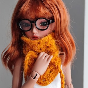 May include: A doll with red hair wearing round black glasses and a yellow crocheted scarf.