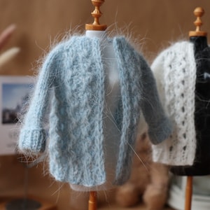 May include: Two fuzzy knit cardigans on display mannequins. The cardigan on the left is light blue and the cardigan on the right is white.