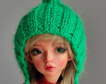 Peut inclure: Un bonnet en tricot vert avec un sommet pointu et de longues oreillettes. Le bonnet est fait d'un fil doux et duveteux et a une coupe ample et décontractée.