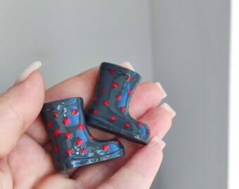May include: A pair of miniature gray rain boots with red polka dots. The boots are glossy and have a rounded toe and a short shaft. The boots are a decorative item.