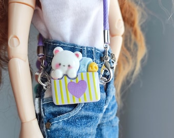 May include: A small, white and yellow striped purse with a purple heart and a cartoon bear design. The purse has a purple strap and silver clasps. The purse is attached to a doll wearing a white top and blue jeans.