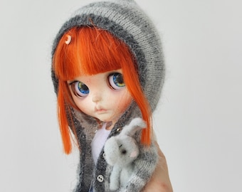 May include: A red-haired doll with blue eyes wearing a gray knitted hooded sweater and holding a gray plush bunny.