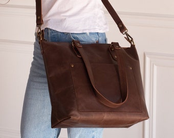 May include: A brown leather tote bag with a long strap. The bag has a front pocket and a top zipper closure.