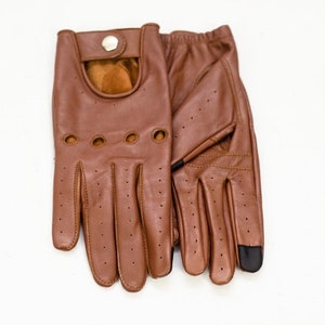 Puede incluir: Un par de guantes de conducir de cuero marrón con detalles perforados y cierre de presión.