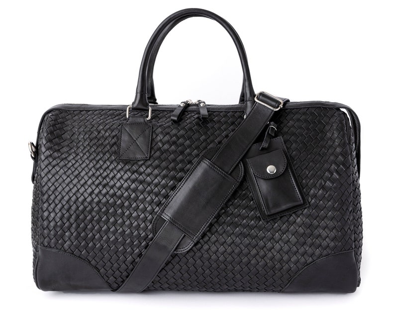 May include: A black leather woven duffel bag with a top handle and an adjustable shoulder strap. The bag has a small zippered pocket on the front.