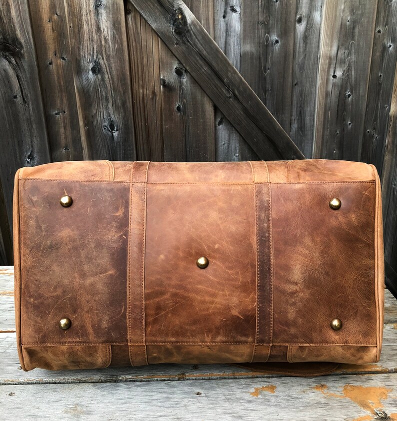 K&ouml;nnte beinhalten: Eine braune Ledertasche mit Messing-Akzenten. Die Tasche hat eine rechteckige Form und ist aus abgenutztem Leder gefertigt.