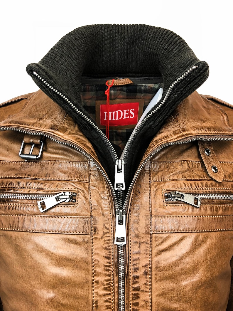 May include: A brown leather jacket with a zipper closure and multiple pockets. The jacket has a dark green knit collar and a red label with the word "HIDES" on it.